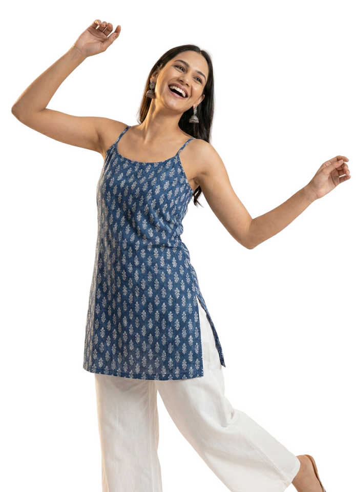 Woman wearing a blue patterned top and white pants against a plain background